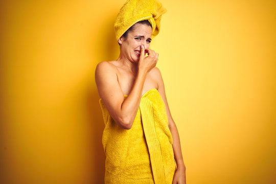 Beautiful Woman Wearing Shower Towel On Body And Head Over Yellow Isolated Background Smelling Something Stinky And Disgusting, Intolerable Smell, Holding Breath With Fingers On Nose. Bad Smell