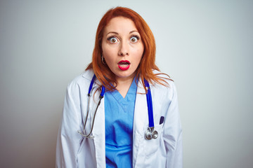 Young redhead doctor woman using stethoscope over white isolated background afraid and shocked with surprise and amazed expression, fear and excited face.