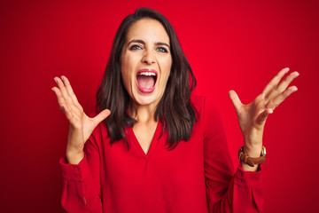 Young beautiful woman wearing shirt standing over red isolated background celebrating mad and crazy for success with arms raised and closed eyes screaming excited. Winner concept