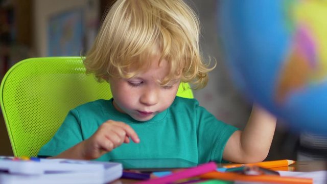 A cute little child uses a tablet PC at a table at home.