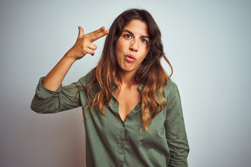 Young beautiful woman wearing green shirt standing over grey isolated background Shooting and killing oneself pointing hand and fingers to head like gun, suicide gesture.