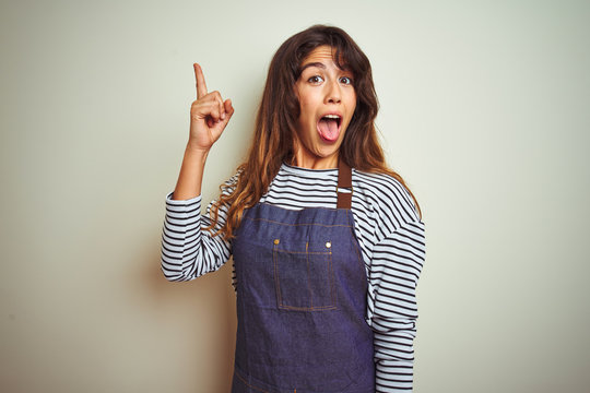 Young beautiful chef woman wearing apron cooking over white isolated background pointing finger up with successful idea. Exited and happy. Number one.