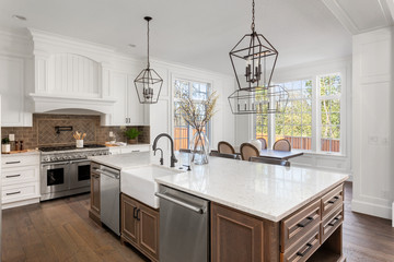 Beautiful kitchen in new traditional style luxury home, with quartz counters, hardwood floors, and stainless steel appliances. Lights are off. 