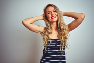 Fototapeta premium Young beautiful woman wearing stripes t-shirt standing over white isolated background relaxing and stretching, arms and hands behind head and neck smiling happy