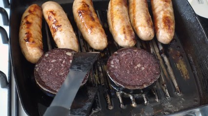 Sausages and black pudding being cooked in a griddle pan 