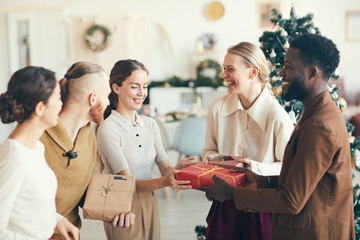 Waist up portrait of cheerful young people exchanging presents during Christmas party in cozy...