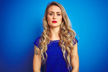 Young beautiful woman standing over blue isolated background with serious expression on face. Simple and natural looking at the camera.