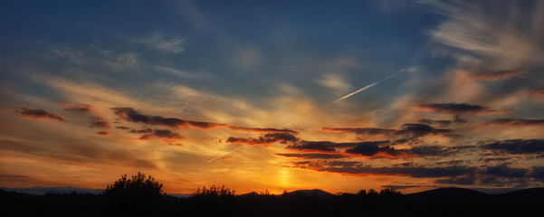 An aircraft vapour trail punches through a colourful sunset