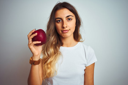 Young beautiful woman eating red apple over grey isolated background with a confident expression on smart face thinking serious