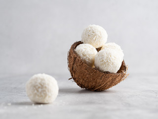 Fototapeta na wymiar Coconut bliss balls in coconut shells on white gray background closeup view