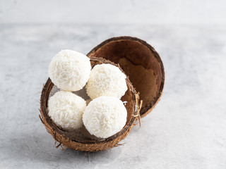 Coconut bliss balls in coconut shells on white gray background closeup view