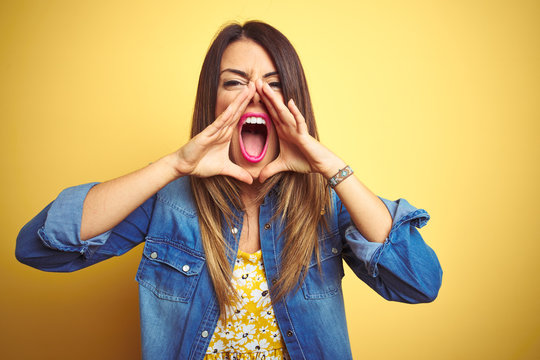 Young beautiful woman standing over yellow isolated background Shouting angry out loud with hands over mouth