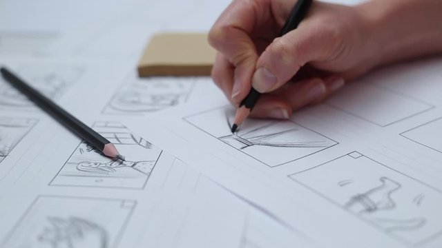 Hands draw with a pencil the storyboard for the film. 