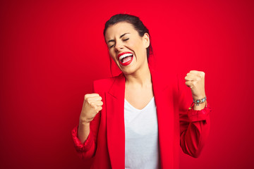 Young beautiful business woman standing over red isolated background very happy and excited doing...