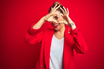 Young beautiful business woman standing over red isolated background Doing heart shape with hand and fingers smiling looking through sign