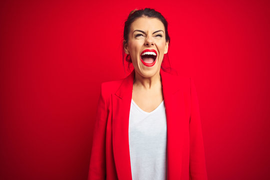 Young beautiful business woman standing over red isolated background angry and mad screaming frustrated and furious, shouting with anger. Rage and aggressive concept.