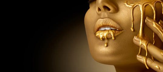 Fototapeta Gold Paint smudges drips from the face lips and hand, lipgloss dripping from sexy lips, golden liquid drops on beautiful model girl's mouth, gold metallic skin make-up. Beauty woman makeup close up obraz