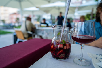 Pitcher and glass of fruity red sangria at an outdoor restaurant with woman at table