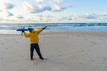 a boy in a bright yellow jacket plays with a plane on a sunny autumn day ha the seashore