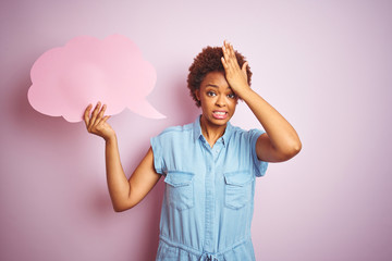 Young african american woman holding speech bubble over pink isolated background stressed with hand...