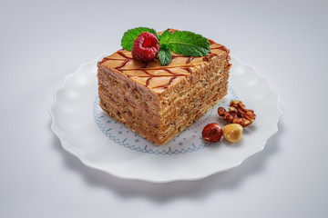 Cake piece with nuts, chocolate, mint and raspberry on a plate isolated on white background