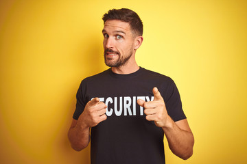 Young safeguard man wearing security uniform over yellow isolated background pointing fingers to camera with happy and funny face. Good energy and vibes.