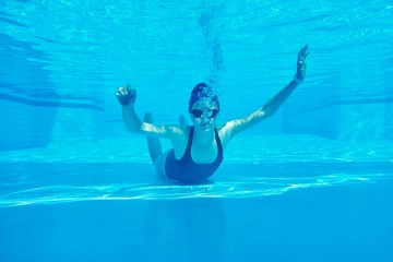 Young girl swimmer in swimsuit with goggles and swimming cap underwater in pool