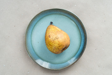 Yellow-bellied pear lies on a blue plate. Autumnal fruit composition.
