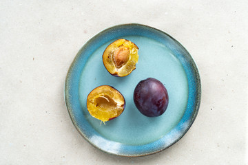 Ripe plums lie on a blue plate. Pieces of purple plum.