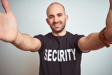 Young safeguard man wearing security uniform over isolated background looking at the camera smiling with open arms for hug. Cheerful expression embracing happiness.