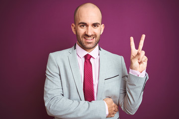 Young business man wearing suit and tie over purple isolated background smiling with happy face winking at the camera doing victory sign. Number two.