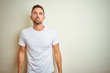 Young handsome man wearing casual white t-shirt over isolated background looking at the camera blowing a kiss on air being lovely and sexy. Love expression.