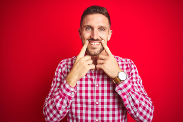 Young handsome man over red isolated background Smiling with open mouth, fingers pointing and forcing cheerful smile