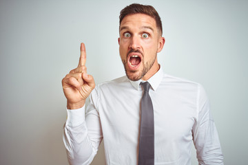 Young handsome business man wearing elegant white shirt over isolated background pointing finger up with successful idea. Exited and happy. Number one.