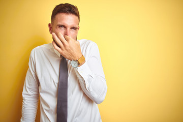 Young handsome business man wearing elegant white shirt over yellow isolated background smelling...