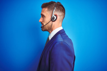 Young handsome operator man wearing call center headset over blue isolated background looking to...