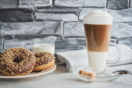 Conceptual delicious sweet breakfast. Latte macchiato coffee  with sweet donuts with a hole and morning newspaper.