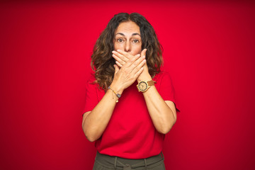 Middle age senior woman with curly hair over red isolated background shocked covering mouth with hands for mistake. Secret concept.