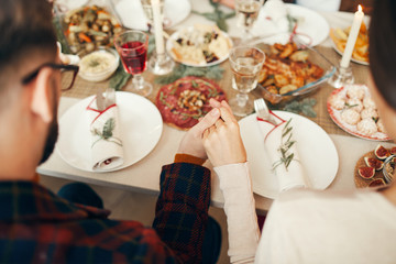 Fototapeta na wymiar Above view close up of people sitting at dining table on Christmas and joining hands in prayer, copy space
