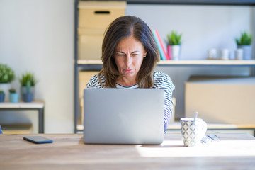 Middle age senior woman sitting at the table at home working using computer laptop skeptic and...