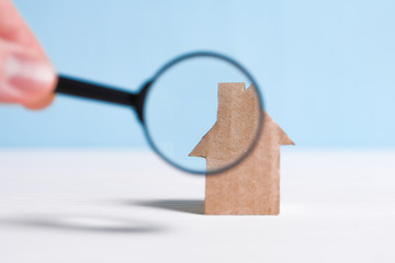 Abstract cardboard house, hand holds a glass magnifier. The concept of checking the home, the...