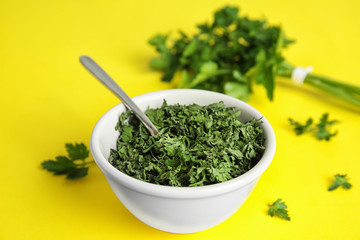 Bowl with spoon and dried parsley on yellow background