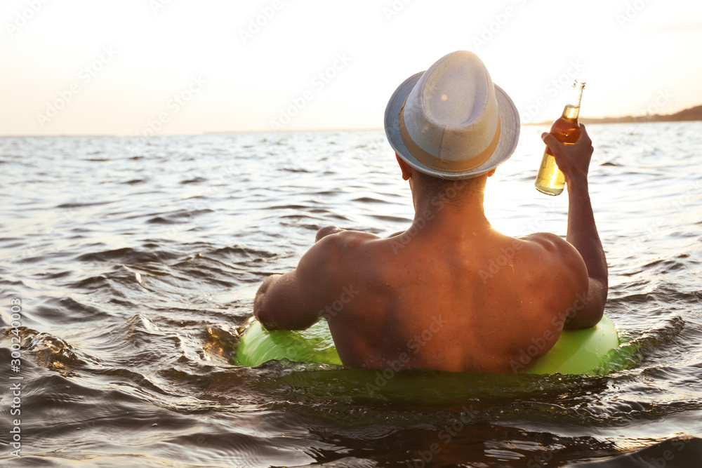 Poster Young man with drink on inflatable ring in sea