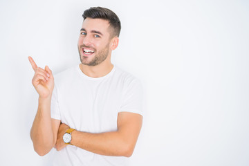 Fototapeta premium Young handsome man wearing casual white t-shirt over white isolated background with a big smile on face, pointing with hand and finger to the side looking at the camera.
