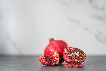 Sliced pieces of pomegranate lie on a black kitchen counter top in the background of marble. Exotic fruit juice ingredient. Culinary Blog Background.