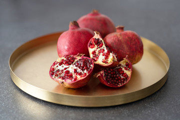 Pomegranate served on a golden tray. Pieces of lumber lie on a plate.