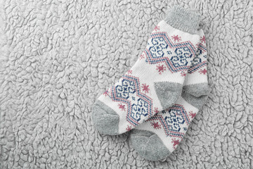 Knitted socks on grey fur background, flat lay. Space for text