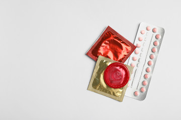 Condoms and birth control pills on light grey background, flat lay with space for text. Safe sex concept