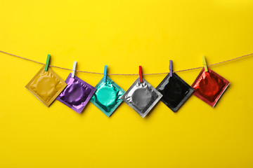 Colorful condoms hanging on clothesline against yellow background. Safe sex concept - obrazy, fototapety, plakaty