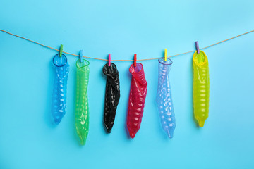Used colorful condoms hanging on clothesline against light blue background. Safe sex concept
